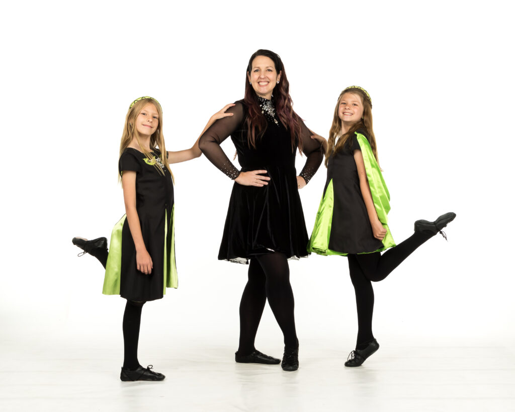Teacher and two young dancers in the ADC Irish Dance Studio showcasing dance costumes.